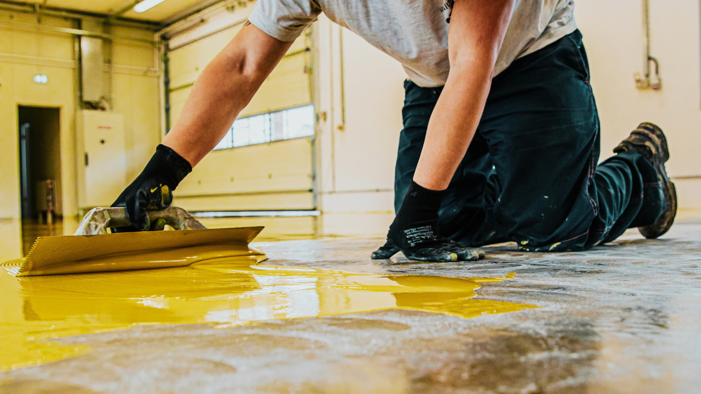 A professional applies vibrant yellow epoxy coatings to a concrete floor in a commercial space, ensuring a durable and polished surface finish.
