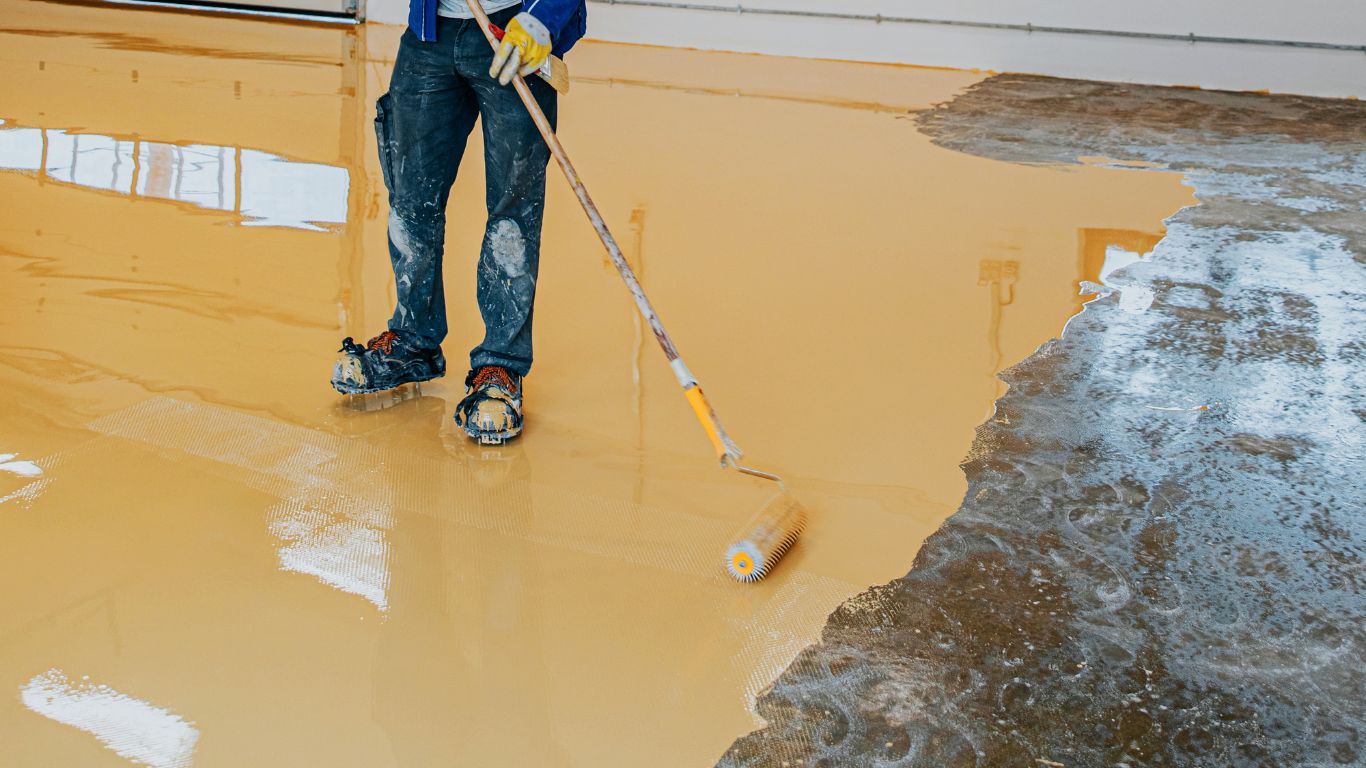 Give Your Garage New Life With Epoxy Coating in Fort Myers Worker applying epoxy coating in Fort Myers on a concrete floor.